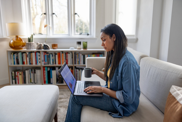 Woman at home using her laptop while drinking a cup of coffee