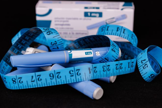 An artistic composition of an Semaglutide box, semaglutide pens, and a blue sewing tape on a dark background, representing diabetes care and precision in health management