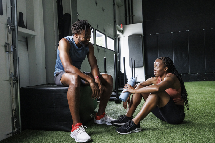 Smiling man and woman talking while taking break from exercise at gym