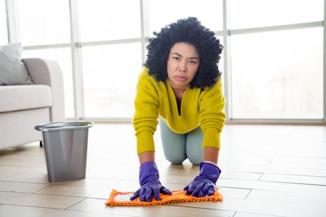 Young woman cleaning her home with a mop and bucket, wearing gloves and casual clothes, representing household chores