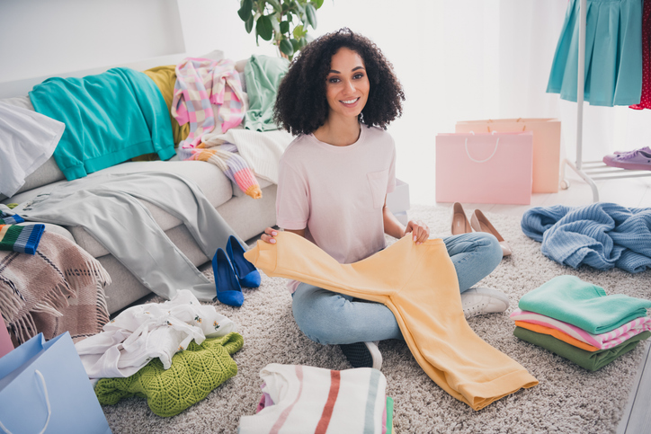 Photo of charming positive cute lovely girl sitting carpet putting clothes preparing trip wardrobe indoors