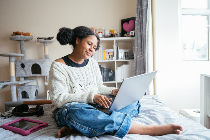 Black teenage schoolgirl using laptop for homeschooling and homework