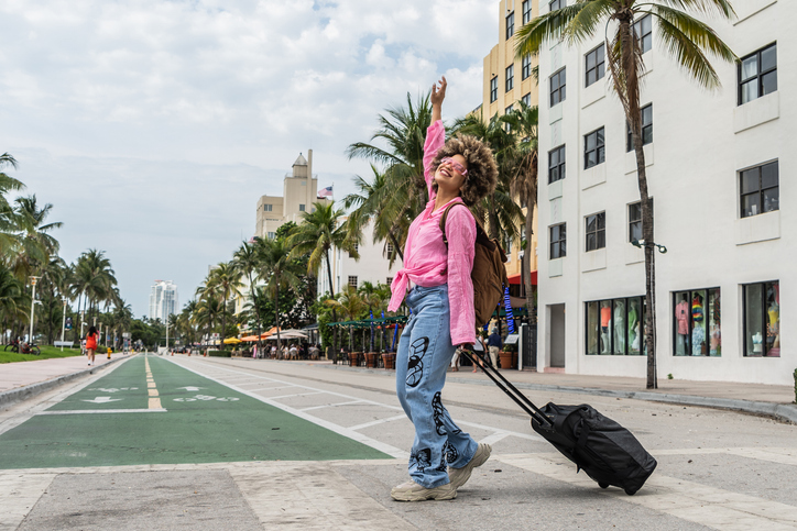 Young Latinx tourist woman with suitcase walking through Miami, USA