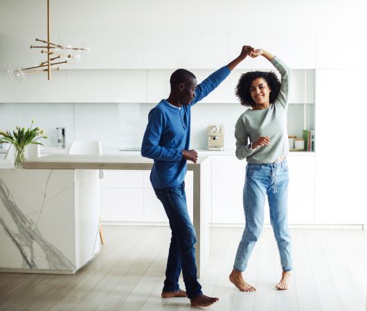 Lovely millennial black spouses having fun together dancing to music in modern kitchen interior.