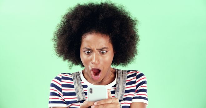 Black woman, smartphone and shock with open mouth in studio, what or fake news with alert for online message. Surprise announcement, alarm or wow expression with WTF on mobile app on green background