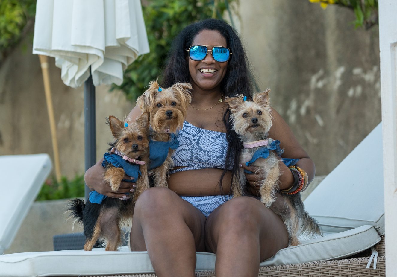 Overweight woman in swimsuit sitting on a deck chair with her 3 puppies