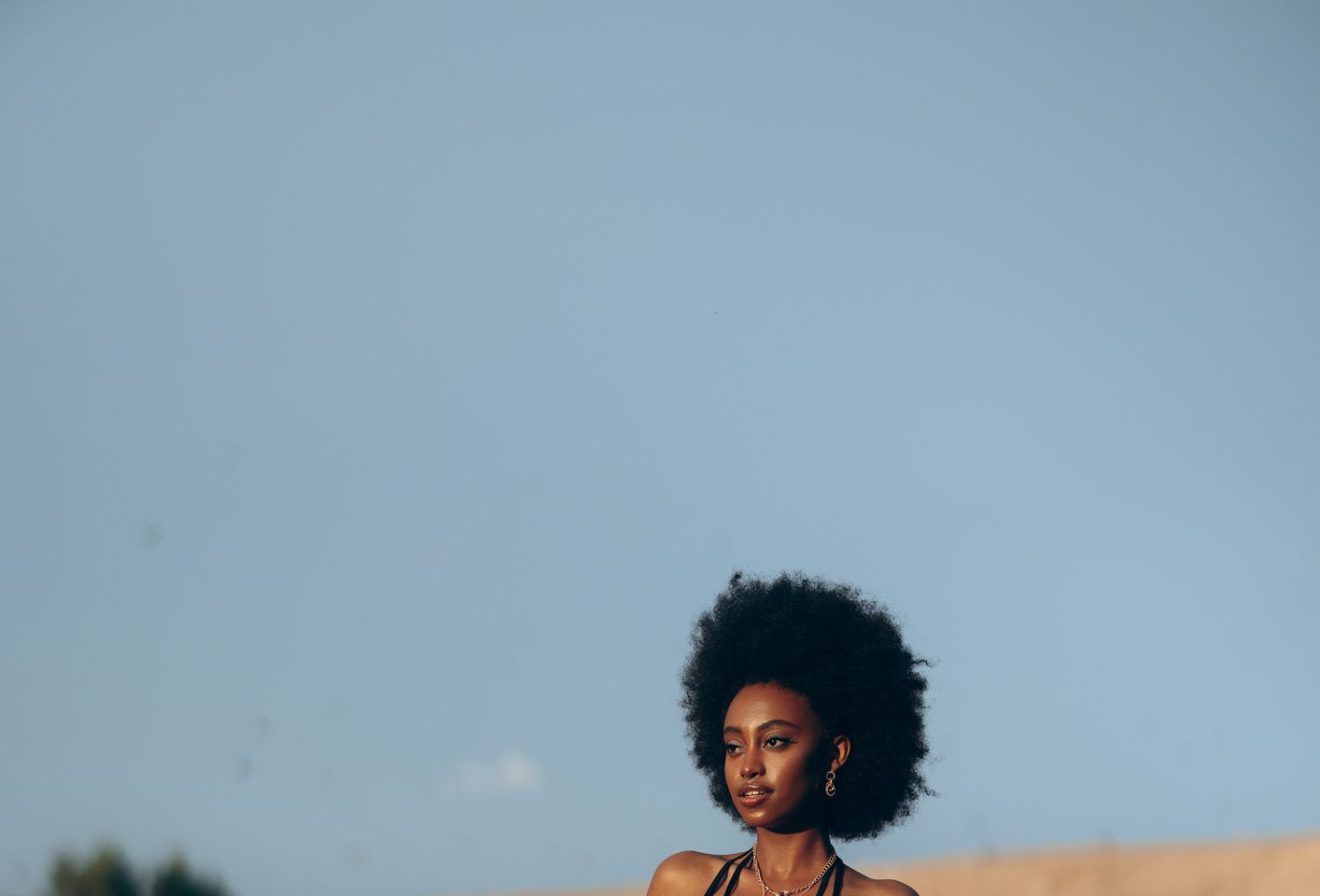 Young african woman sitting on top of a pickup truck against background of sandy canyon and sky.