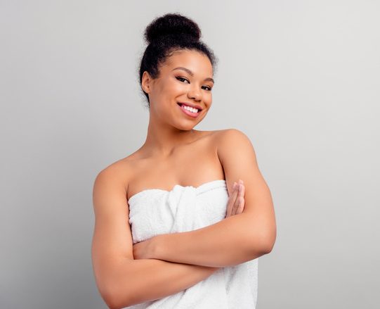 Confident young African American woman in towel posing against a gray background showcasing natural beauty