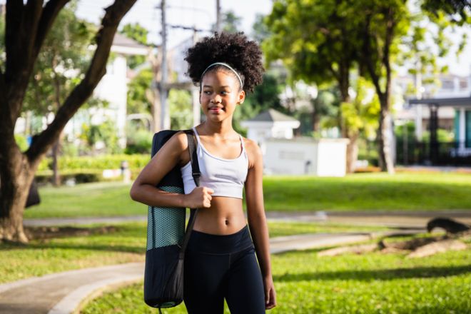 African American girl carrying exercise mat outdoors in park with confident expression and natural hairstyle on sunny day