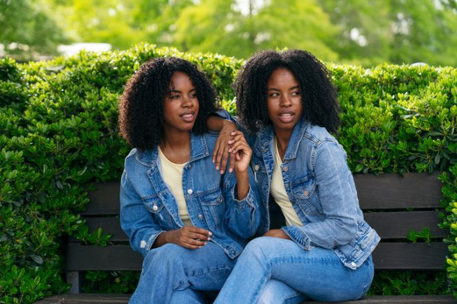 Twin sisters holding hands and sitting on bench in park