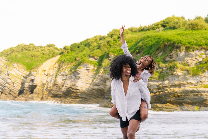 Happy couple piggybacking on the beach, enjoying summer vacation
