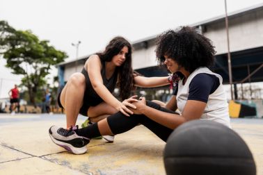 Basketball player woman helping injured friend on a sport court