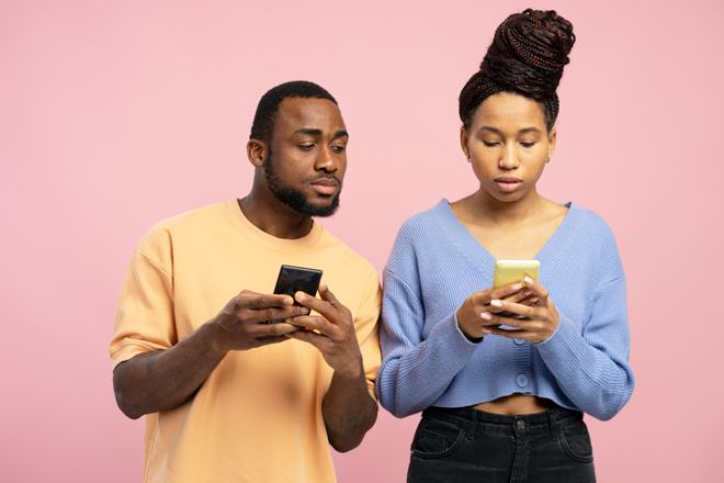 Curious man peeking at woman's phone on pink background