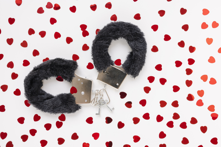 Adult handcuffs sex toy on Valentines Day with hearts background. Closeup, copy space