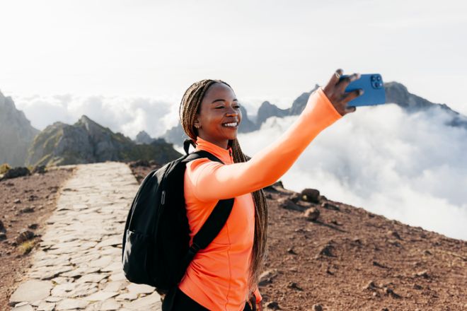Young woman with a backpack and long braids taking a selfie with her cell phone on a hiking trail
