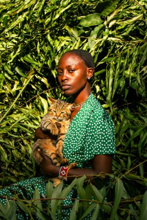 Young African Woman in Green Dress Holding Cat Among Eucalyptus Leaves