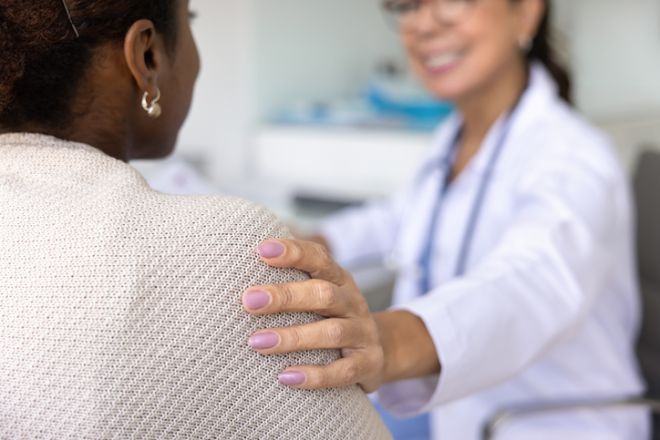Doctor gently places hand on shoulder of woman patient, closeup