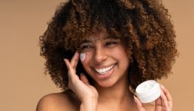Beautiful black woman applying face luxury sunscreen or moisturizer cream for perfect hydrated healthy fresh skin care - Cosmetic dermatology product concept