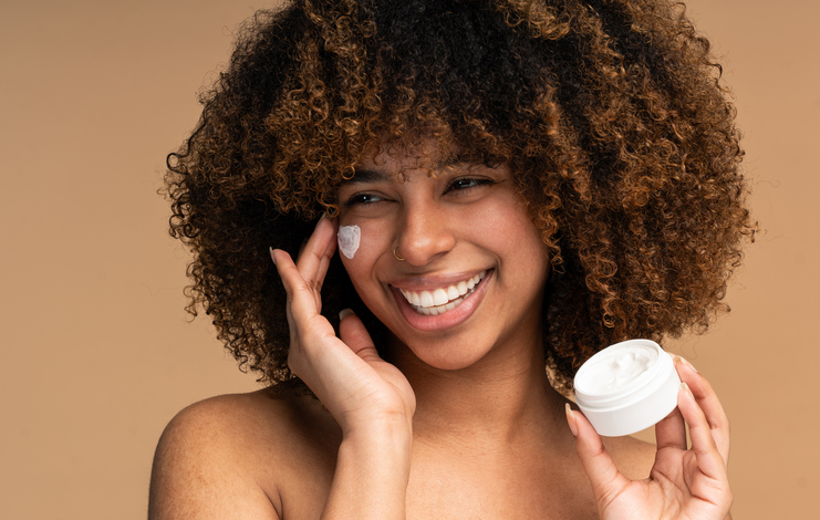 Beautiful black woman applying face luxury sunscreen or moisturizer cream for perfect hydrated healthy fresh skin care - Cosmetic dermatology product concept