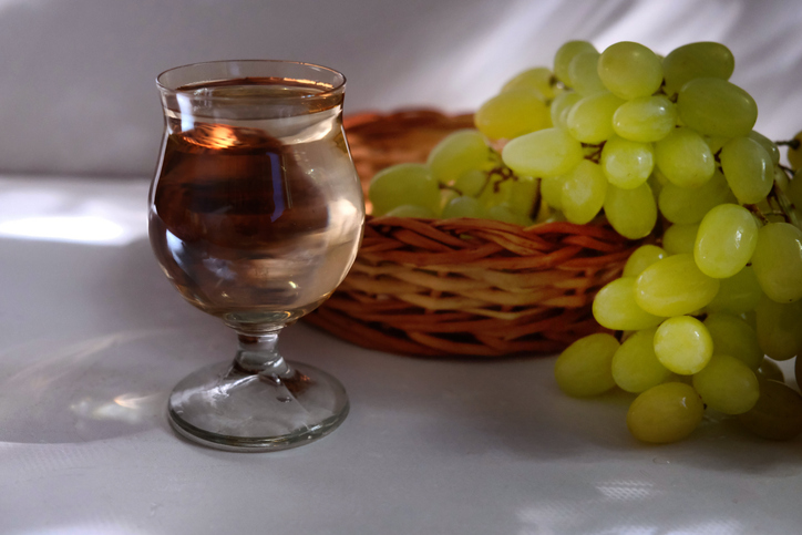 Portuguese green wine Vinho Verde and bunch of green grapes in the wicker basket. Crystal glassware. Bar counter. Sunlight and shadows on the white table, wall. The warm light of the golden hour.