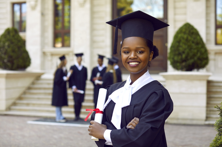 Happy smiling afroamerican woman in graduation gown and cap graduates universuty looking at camera.