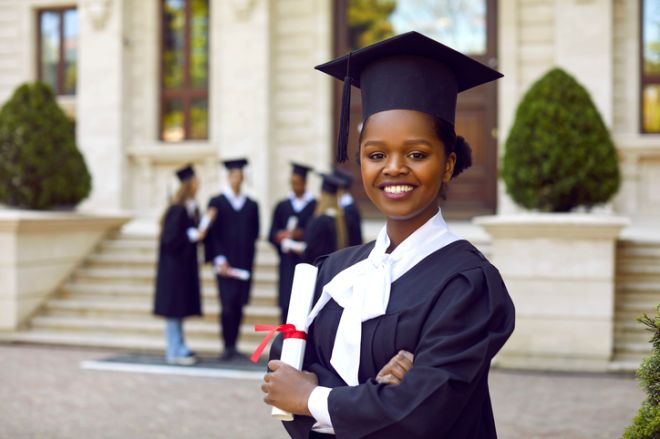 Happy smiling afroamerican woman in graduation gown and cap graduates universuty looking at camera.