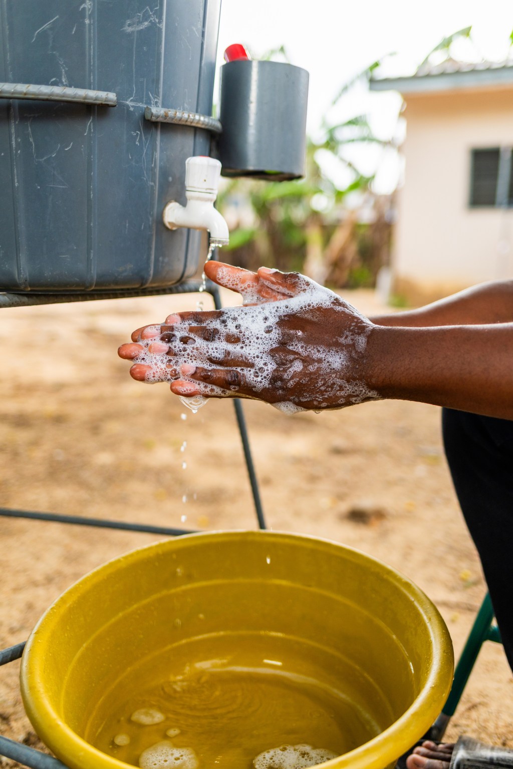 African man in wheelchair washing hands with Veronica bucket outdoors for hygiene and disease prevention
