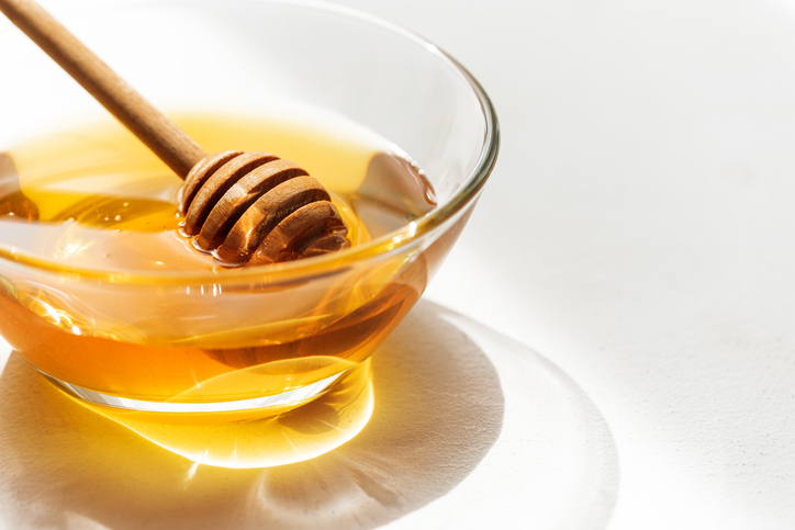 Golden Honey in Glass Bowl with Wooden Dipper on White Background