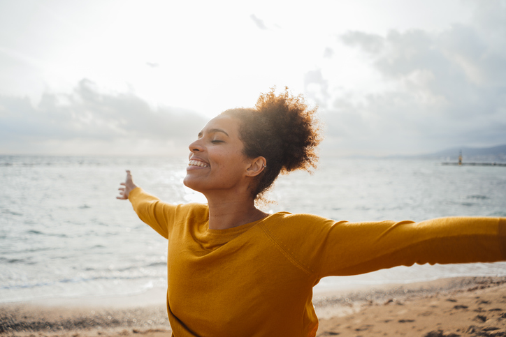 Smiling carefree woman with arms outstretched having fun at beach
