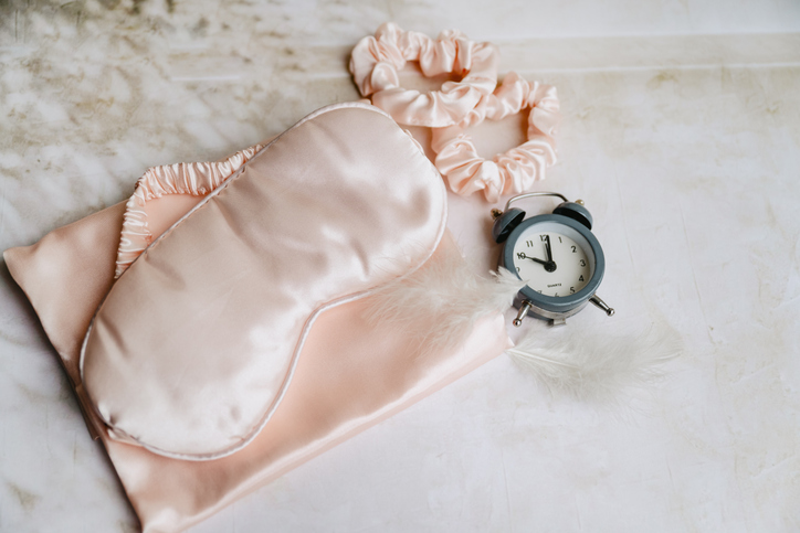Silk sleeping mask and feathers on shadows background