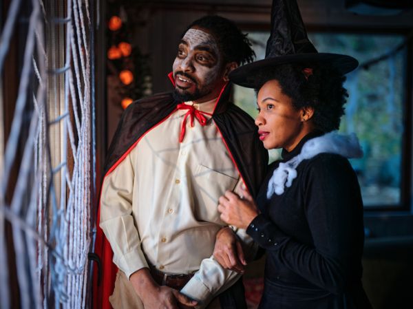 Black couple in Halloween costumes looking through window at home.