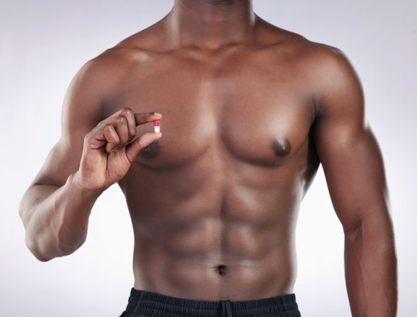 Cropped shot of an unrecognsiable man standing alone in the studio and holding a supplement pill