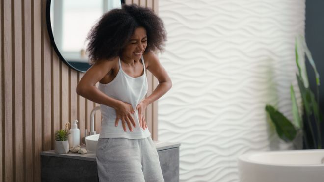 African American ill sick unwell sad woman with stomach ache standing in bathroom at home in bath biracial ethnic girl suffering abdominal pain painful periods menstruation digestion health problem