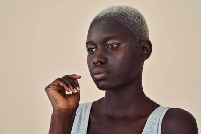 Cool gen z African girl with short blond hair looking away at beige background.
