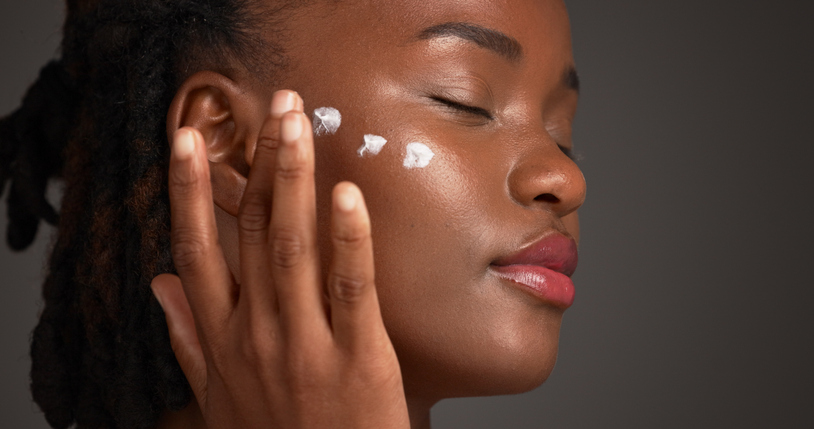 Black woman, studio and skincare with lotion for moisturizer or face cream on a gray background. Female person, model or applying product with beauty cosmetics for anti aging or soft skin on space