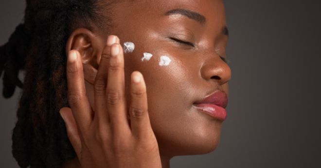 Black woman, studio and skincare with lotion for moisturizer or face cream on a gray background. Female person, model or applying product with beauty cosmetics for anti aging or soft skin on space