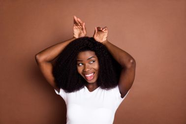 Portrait of excited cheerful dark skin girl arms palms make bunny ears look empty space isolated on brown color background