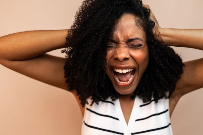 Mid adult woman expressing anger and irritation against beige background