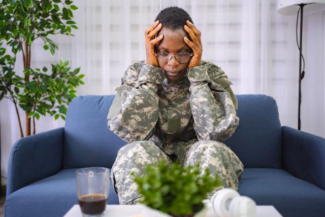 Depressed african american soldier suffering from ptsd sitting on sofa
