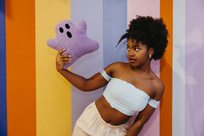 Young Black woman holding a plush ghost toy in colorful Halloween-themed space