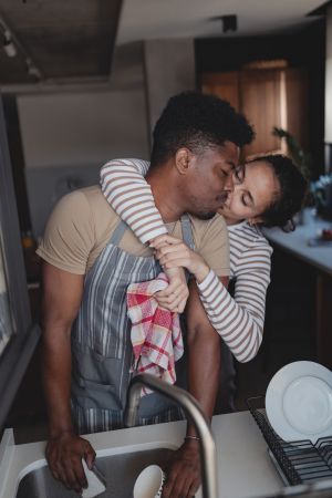 Happy couple in the kitchen sharing a playful moment while doing the dishes, with the woman hugging the man from behind.