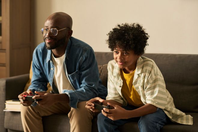 Father and son playing video game together at home on sofa
