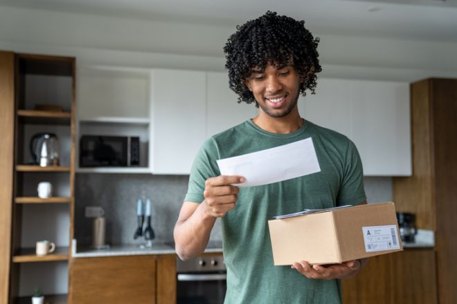 Man at home receiving the mail and reading a letter while holding some packages