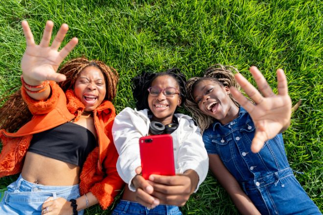 Young diverse women friends lying on grass taking selfie