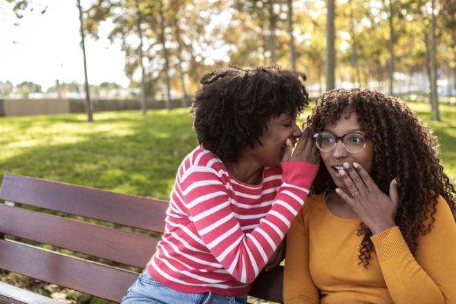 Women whispering secret, gossip, and surprise in park