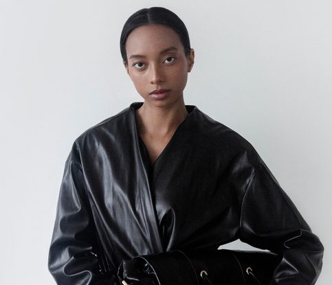 Beautiful young woman wearing unique designer outfit Leather jacket coat and holding a bag Stylish girl of mixed ethnicity African American Asian natural beauty Fashion model studio portrait on white background Luxury clothes Confident look