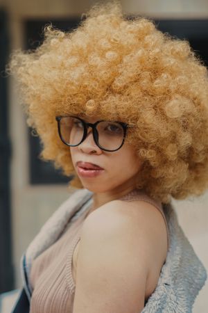 Young woman with blonde afro hair and glasses looking over her shoulder