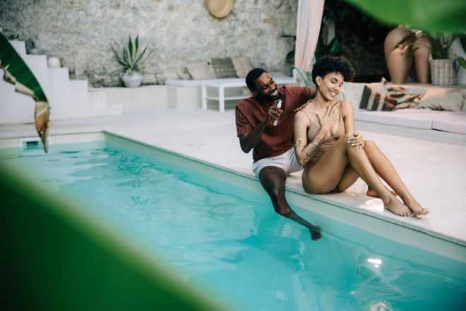 Young Couple Sitting by the Pool, Man Applying Sunscreen to Woman
