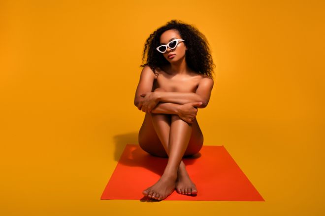 Gorgeous young woman with fashionable sunglasses posing against a vibrant orange background