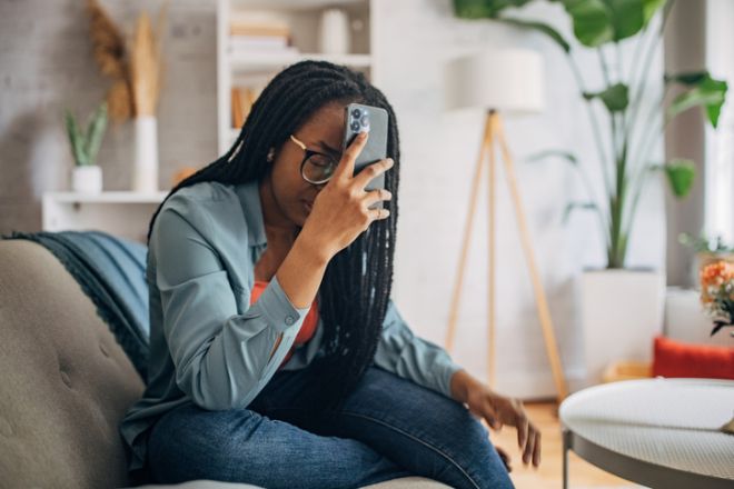 Thoughtful woman with phone in hand at home